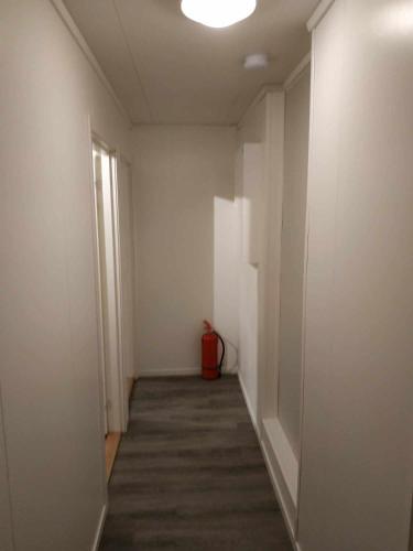 a hallway with a white wall and a red trash can at apartament by the sea in Havøysund