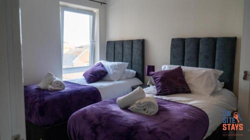 a bedroom with two beds with purple sheets and a window at OnSiteStays - 2 Bedroom Apartment with Ensuite, Free Parking & Wi-Fi in Gravesend
