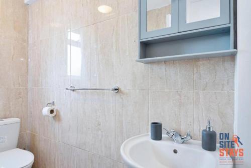 a bathroom with a sink and a toilet and a mirror at OnSiteStays - Comfortable Contractor Accommodation, 3-BR House, WIFI, Parking & Large Garden in Enfield Lock