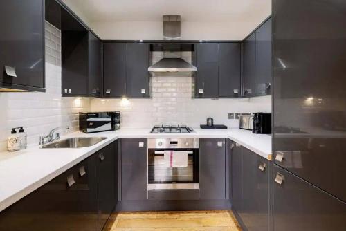 uma cozinha com armários pretos e um forno com placa de fogão em Bright and Quiet 2-bed 2-bath with Great Patio em Londres