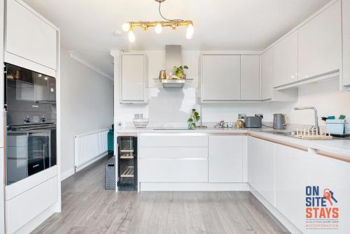 a white kitchen with white cabinets and a wooden floor at OnSiteStays Welling, Modern 2 Bed House, Free Parking & Wifi in Welling