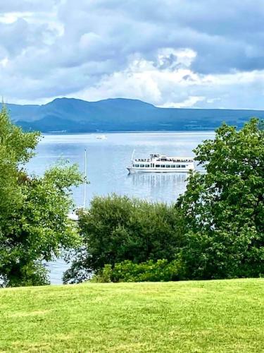a boat on a large lake with trees at Loch View at Lomond Castle in Balloch