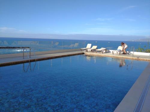 a woman sitting in a chair next to a swimming pool at Apartamento en primera línea de playa in Puerto de la Cruz