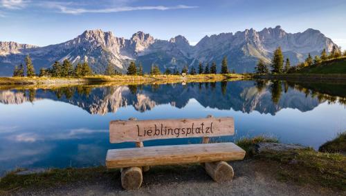 a bench sitting in front of a lake with mountains at Hotel AlpenSchlössl in Söll