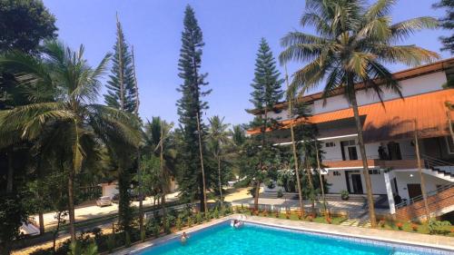 a pool in front of a building with palm trees at Mazra Retreat, Coorg Kushālnagar in Kushālnagar