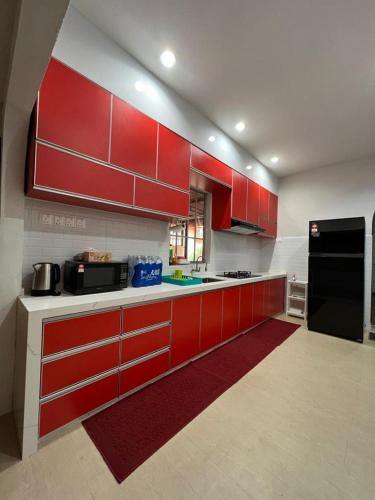 eine Küche mit roten Schränken und einem schwarzen Kühlschrank in der Unterkunft Teratak LS Homestay in Kubang Semang