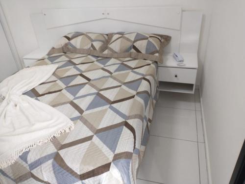 a white bedroom with a bed and a night stand at Flat São Vicente 5 minutos da praia in São Vicente