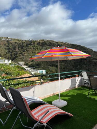 eine Terrasse mit Stühlen und einem Sonnenschirm auf dem Rasen in der Unterkunft Pana House in Calheta