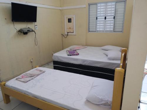 two beds in a small room with a tv at Casa de hospedagem in Aparecida