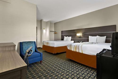 a hotel room with two beds and a blue chair at SureStay Plus Hotel by Best Western Tulsa East in Tulsa