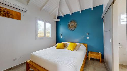 a bedroom with a blue wall and a bed with yellow pillows at Les maisons Cane in Sainte-Rose