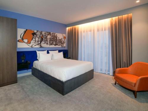 a bedroom with a bed and an orange chair at Novotel Bishkek City Center in Bishkek
