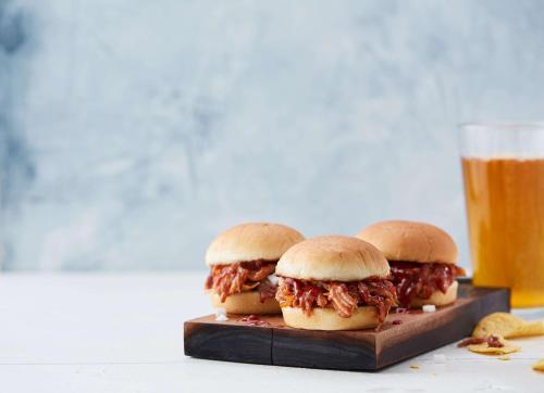 three pulled pork sandwiches on a wooden plate next to a glass of beer at Drury Inn & Suites Huntsville Space & Rocket Center in Huntsville