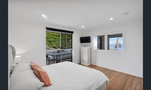 a white bedroom with a bed and a window at Bribie Waters Apartment in Bongaree