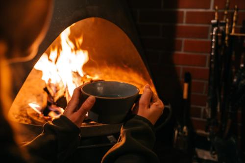a person holding a coffee cup in front of a fireplace at Alpenglow Lodges Ginkei in Niseko