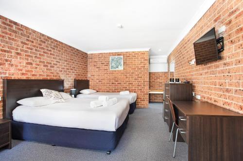 Lake Macquarie Motor Inn في بيلمونت: سريرين في غرفة مع جدار من الطوب