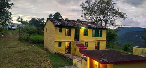 een klein geel huis met een veranda op een veld bij Himalayan and Nature View Homestay in Almora