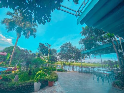 a patio with tables and chairs and palm trees at D&D riverside Homestay in Xuân Sơn
