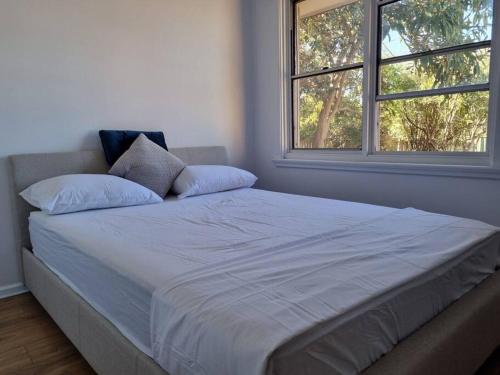a white bed with two pillows and two windows at Close to nature, close to city in Kingston 