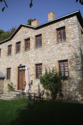 a stone building with chairs and an umbrella in front of it at Guesthouse Kontogianni - Materka in Nymfaio