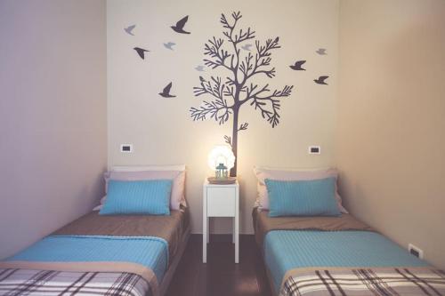 2 Betten in einem Zimmer mit Baum und Vögeln an der Wand in der Unterkunft Villa Lidia in Balestrate