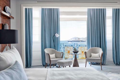 a bedroom with a bed and chairs and a large window at Hôtel Martinez, in The Unbound Collection by Hyatt in Cannes