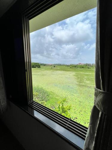 a window with a view of a field of grass at Neville's Villa - Pet friendly with Pool in Alibaug