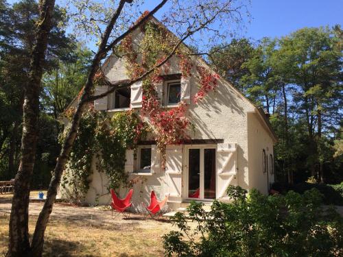 a white house with red chairs in front of it at Chambres au coeur du Massif des Trois Pignons in Noisy-sur-École