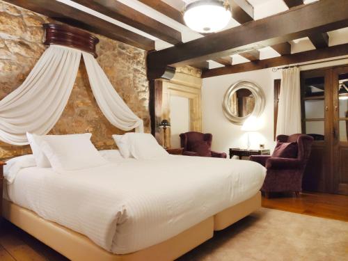 a bedroom with a large white bed and chairs at Hotel Casa del Marqués in Santillana del Mar