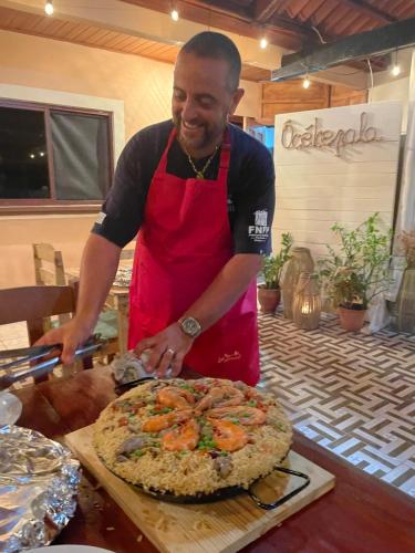 a man in a red apron cutting a pizza at Sea view hills bungalow in Torio