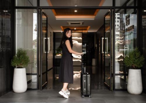 バンコクにあるSAM E Hotel Bangkok Sathornのスーツケースを持つ建物前に立つ女性