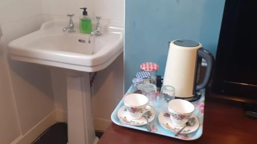 un bagno con lavandino e un vassoio con tazze di Kingsway Bed & Breakfast a Broxbourne