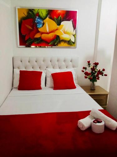 a bedroom with a white bed with red pillows and a painting at Hostal De la 8 in Barranquilla