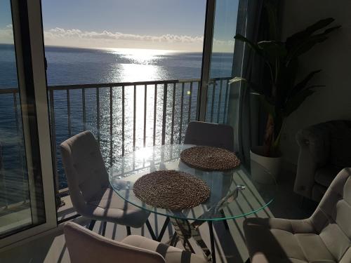 einen Balkon mit einem Glastisch, Stühlen und Meerblick in der Unterkunft Impresionante in Maspalomas
