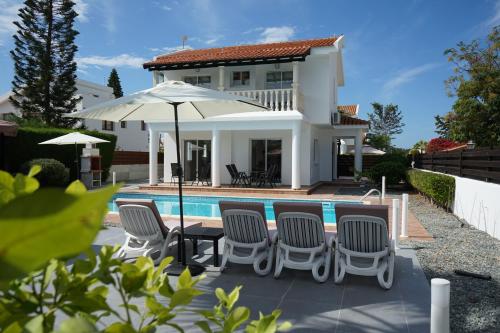 a house with a pool and chairs and an umbrella at Villa Coral Cove in Peyia