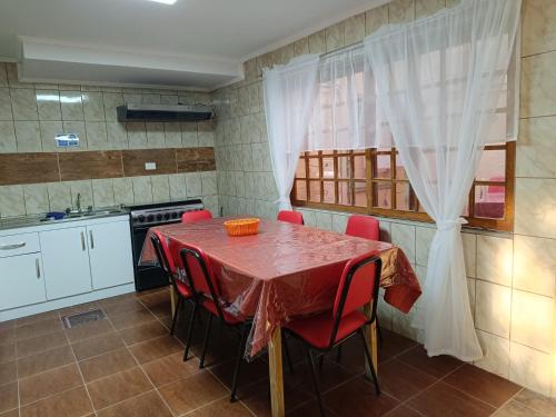 una cocina con mesa con sillas rojas y fregadero en Hostal Ollague, habitaciones con baño privado, en Calama
