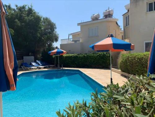 a swimming pool with two umbrellas next to a building at Kato Paphos 2 Bedroom House - Tourist location in Paphos City