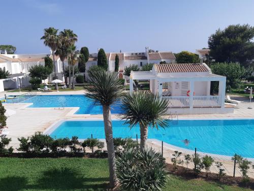 a villa with a swimming pool and palm trees at Son Xoriguer appartement calme, mer, piscines.Son Xoriguer quiet apartment, sea, swimming pools. in Son Xoriguer