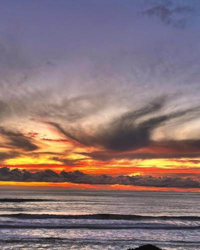 a sunset over the ocean with clouds in the sky at View With A Room NZ - Boutique Beachfront Accommodation on the Great Coast Road in Runanga