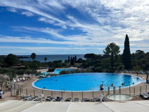 une grande piscine bleue avec des chaises et l'océan dans l'établissement Appartement 2 pièces climatisé en rez-de-jardin Cap Esterel Agay, à Agay