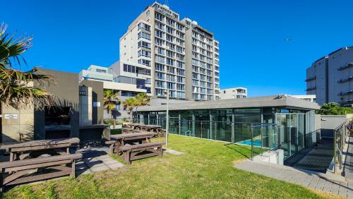 a park with benches and a tall building at Infinity LG8 Beachfront Apartment in Bloubergstrand
