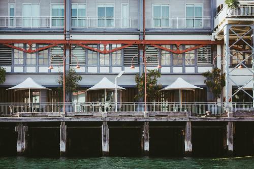 a building with tables and umbrellas next to the water at Pier One Sydney Harbour, Autograph Collection in Sydney