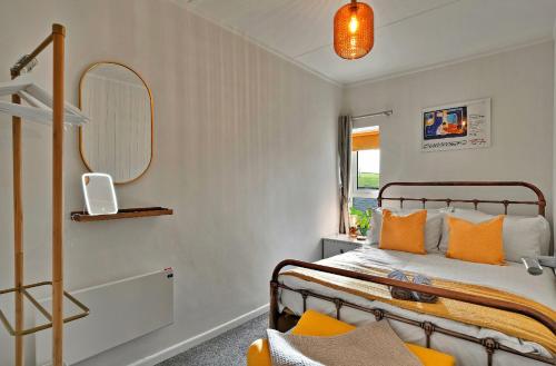 1 dormitorio con 1 cama con almohadas de color naranja y espejo en Beautiful Cottage Short Walk To Porth Beach en Newquay