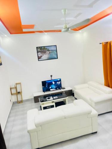 sala de estar con 2 sofás blancos y TV en Charly-Calavi Appartement, en Ouékè-Zoumè