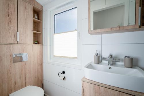 uma casa de banho com um lavatório, um WC e uma janela. em Ostseecamp Lübecker Bucht Haus "Morgensonne" mit überdachter Veranda em Scharbeutz