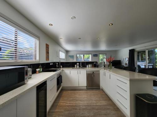 a large kitchen with white cabinets and a large window at Hahei Ocean's 76 in Hahei