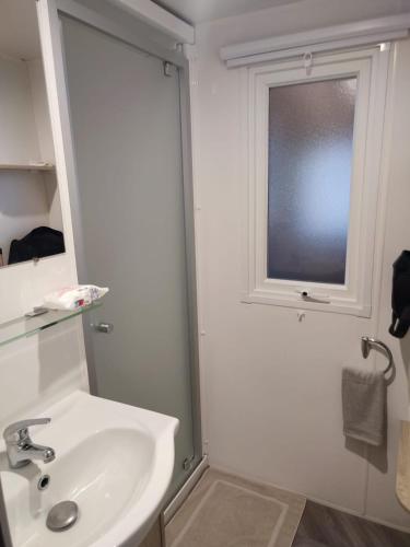 une salle de bain blanche avec un lavabo et une fenêtre dans l'établissement superbe mobil home 6/8 pers,clim, sans vis a vis dans camping 4* espace aquatique, à Vias
