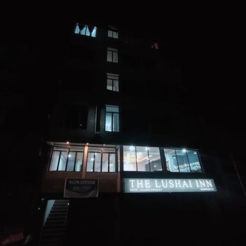 un bâtiment avec un panneau devant lui la nuit dans l'établissement THE LUSHAI INN, à Aizawl