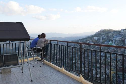 Dos personas sentadas en un balcón con vistas a la ciudad en THE LUSHAI INN en Āīzawl