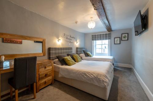 a bedroom with two beds and a desk and a tv at Crown and Cushion Appleby in Appleby